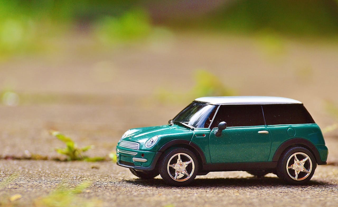 our-services-1 Green toy Mini Cooper car on pavement featuring a shallow depth of field outdoors.